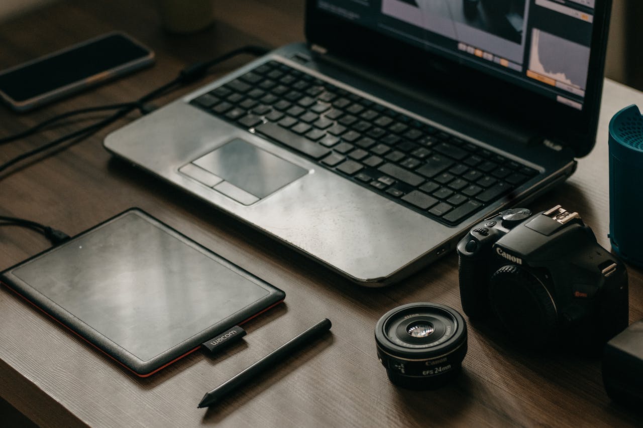 About Laptop, camera, lens, and graphic tablet on a desk for digital creatives.