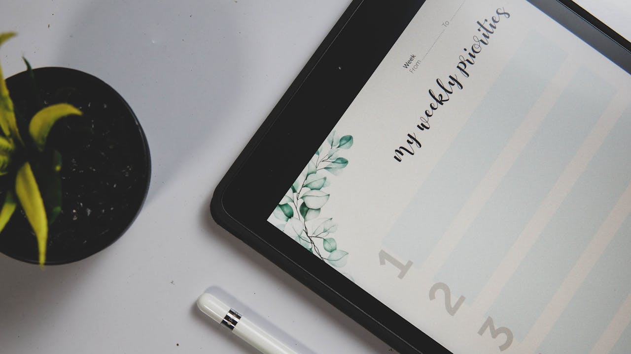 Crafting Captivating Headlines: Your awesome post title goes here Close-up of a tablet displaying a weekly planner with a stylus and a potted plant on a desk.